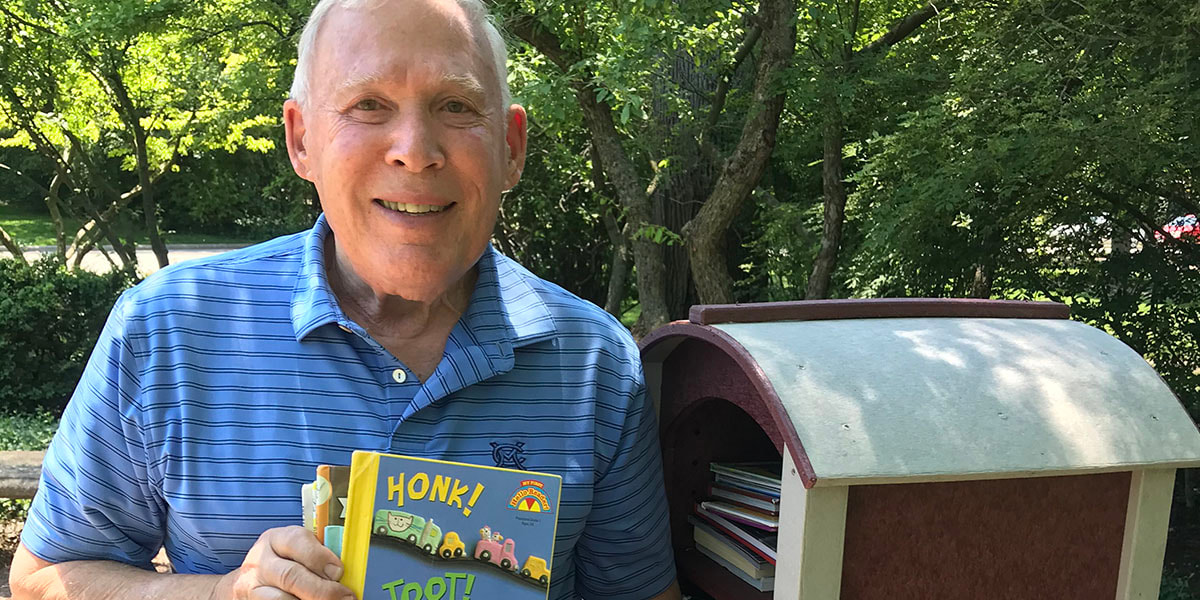 Photo of Jeff Wadler holding a children's picture book, standing beside a Little Free Library in Lincolnshire, Illinois