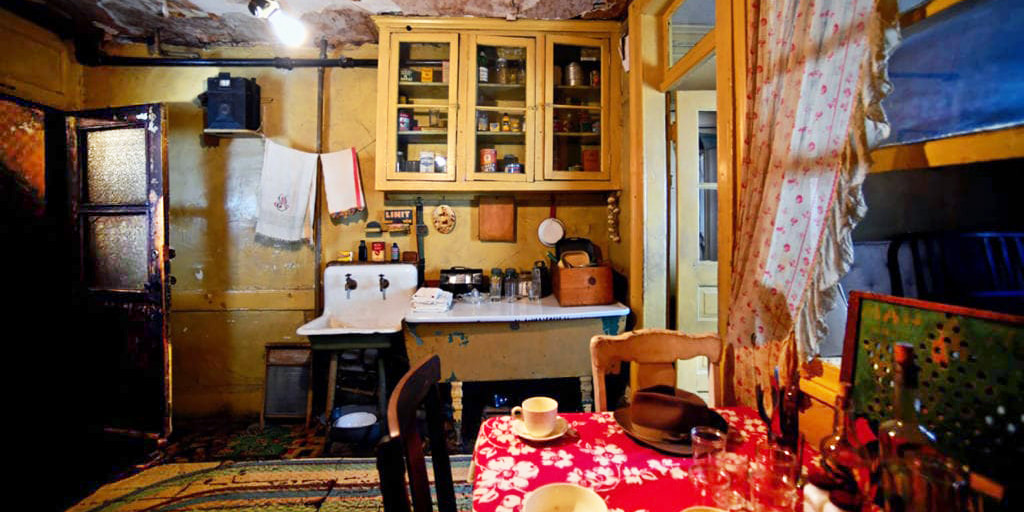 photo of a room at the Tenement Museum in NYC showing a humble kitchen area and a table, bare lightbulb hanging from ceiling
